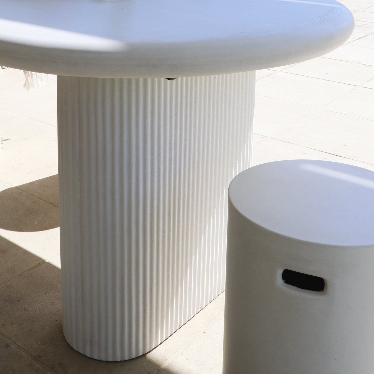 White textured pedestal base table and coordinating stool on a light tiled floor