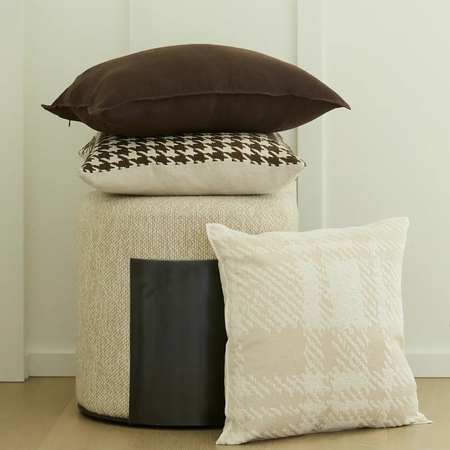 Three cushions on a cylindrical ottoman against a white wall.