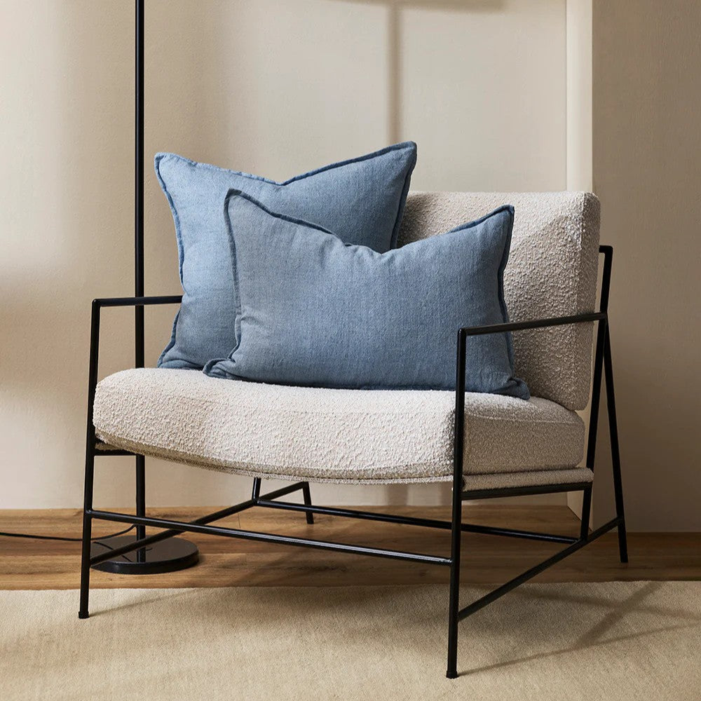 Modern chair with chambray blue linen cushions and a black floor lamp against a beige wall.