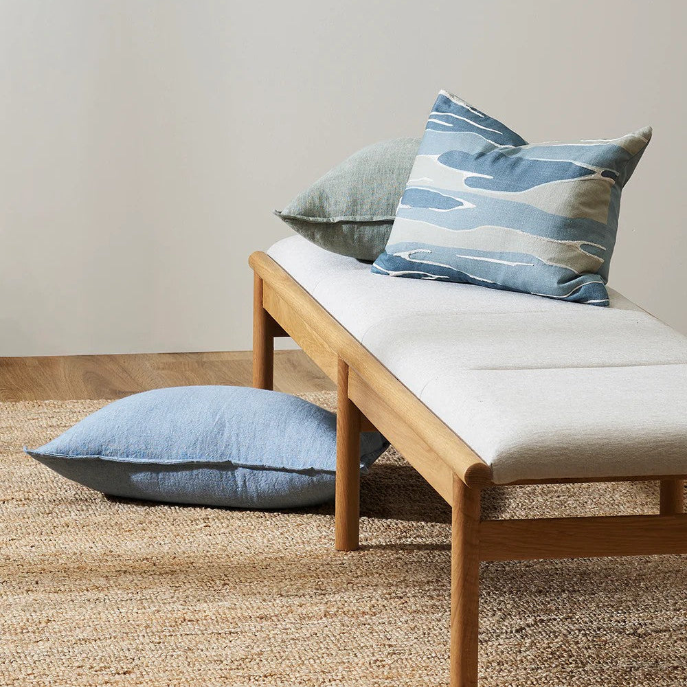 Upholstered seat on wooden bench showing a patterned cushion and a chambray blue linen cushion on the floor.
