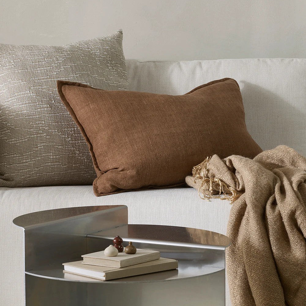 Neutral sofa with a chestnut brown and textured cushion, and a small table with books and decor items.