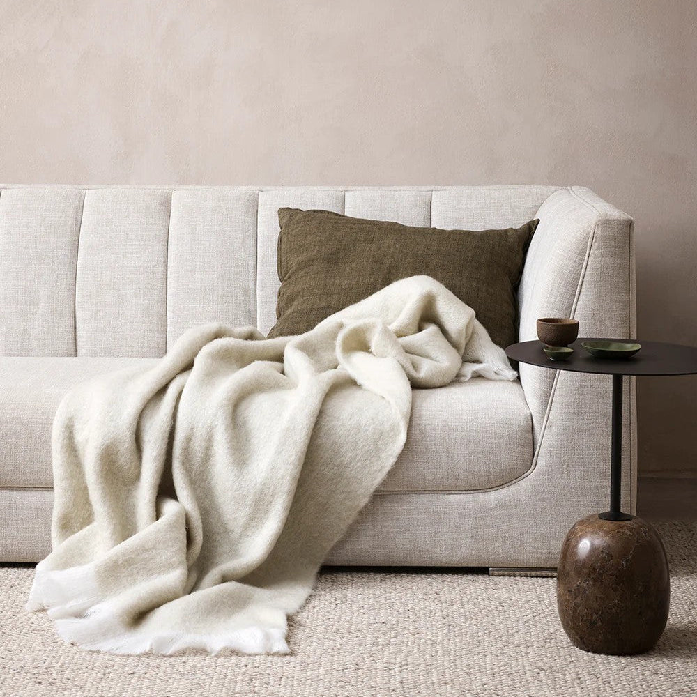 Beige sofa with a white blanket and clove linen cushion in a neutral living room.