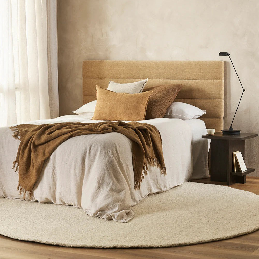 Neatly made bed with tan headboard and cumin linen cushion on a natural linen duvet in a bedroom setting.