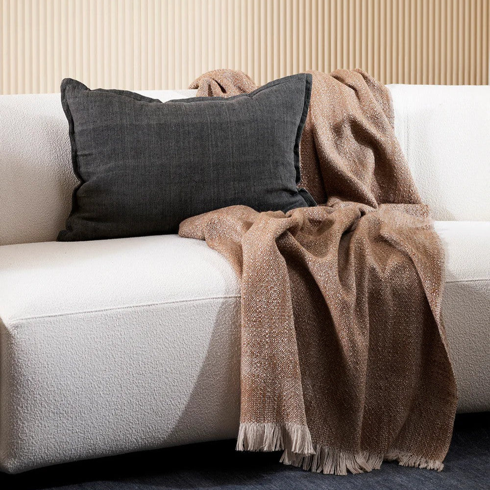 White boucle sofa with a brown blanket and slate grey linen cushion against a beige wall.