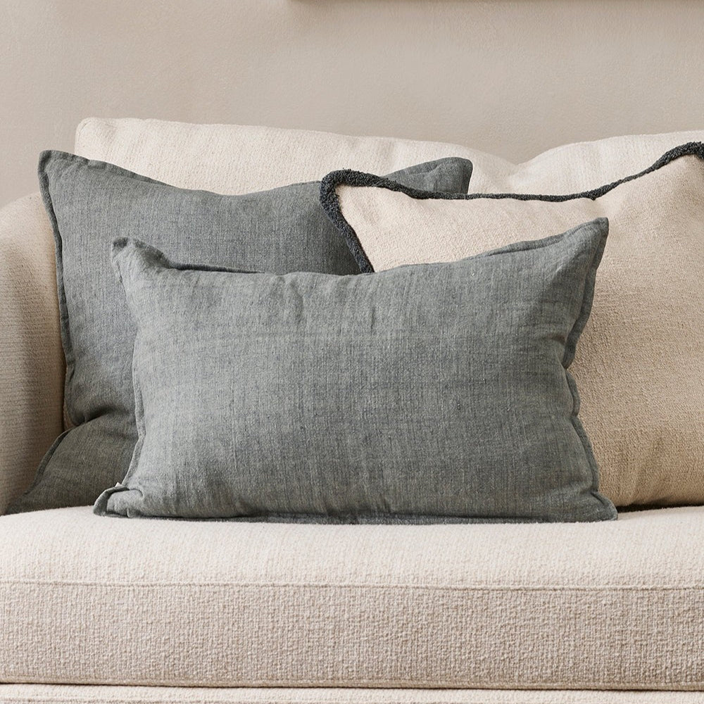 Steel gray linen cushions on a beige sofa with a neutral wall and painting in the background