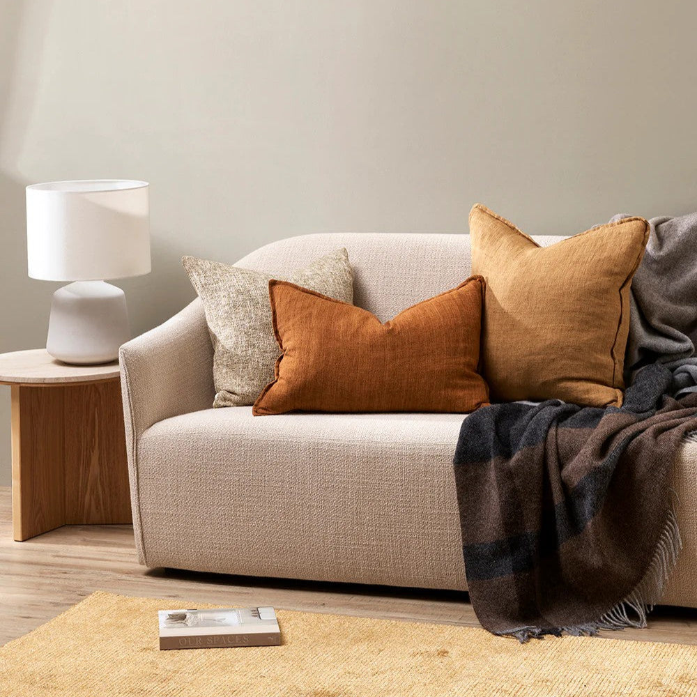 Cosy living room with a beige sofa, tobacco cushions, and a lamp on a wooden side table.