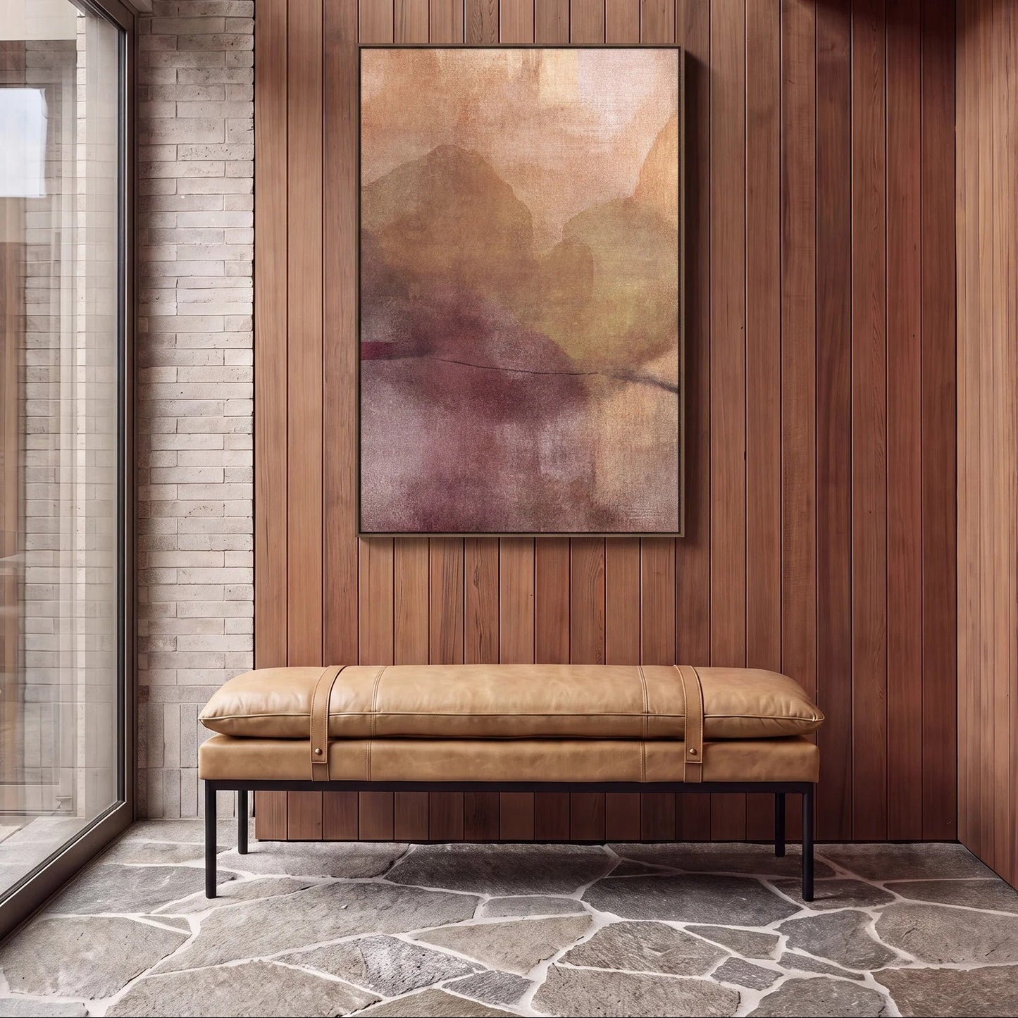 A framed abstract landscape painting with soft beige, brown, and muted purple tones hangs on a wood-panelled wall above a tan leather bench seat in a modern interior setting.