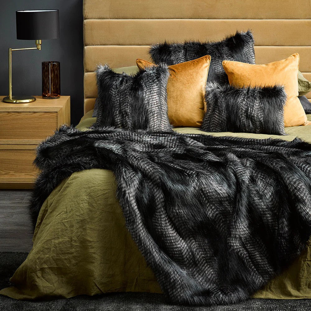 Bedroom with a bed featuring black coyote and orange cushions with a black coyote faux Fur throw blanket, and a nightstand with a lamp.