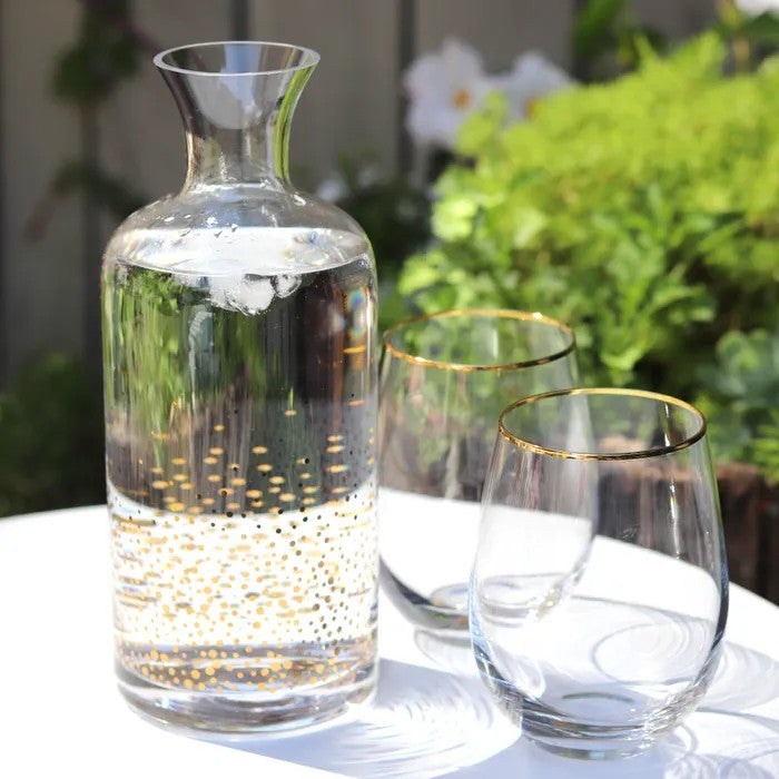 Clear glass carafe with gold dots displayed with two coordinating glasses on a table outdoors.