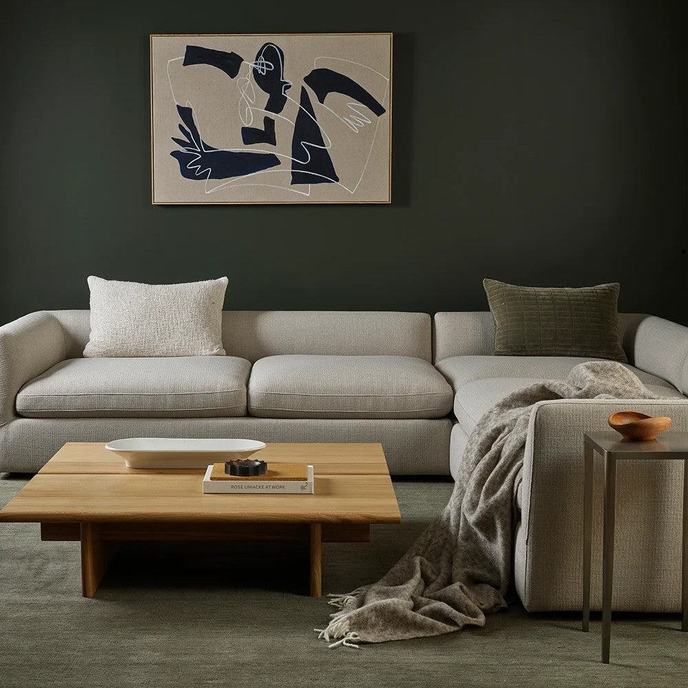 Living room with a beige sectional sofa, wooden coffee table, wool throw and abstract art on the wall.