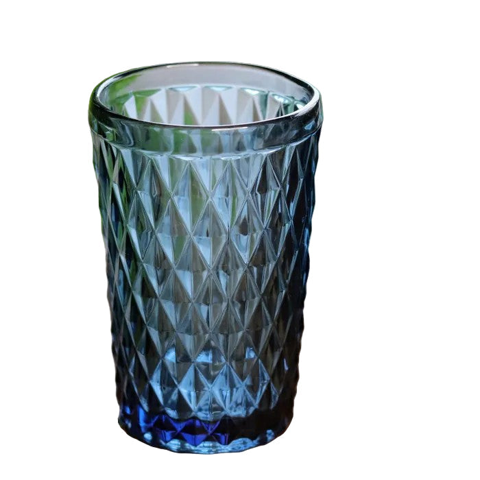 Blue textured glass tumbler on a wooden surface with green leaves in the background