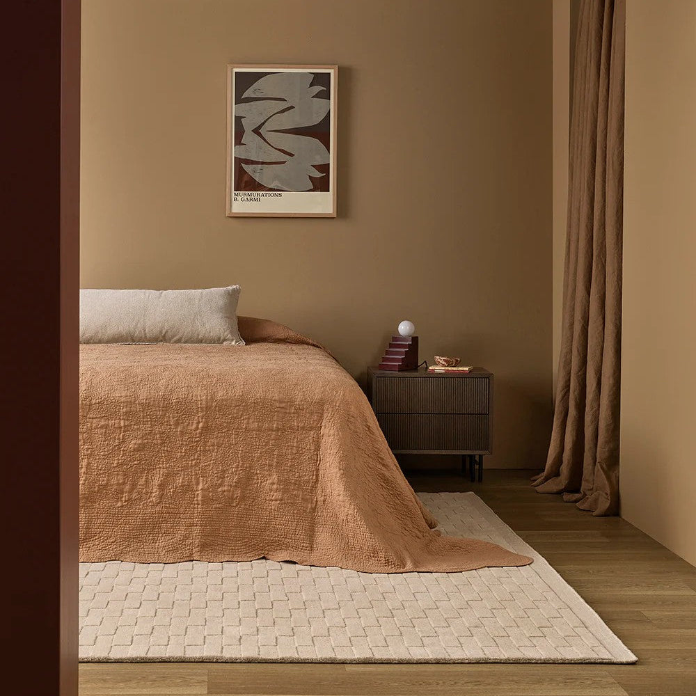 Cozy bedroom with ginger bedspread, nightstand, almond patterned floor rug and abstract art on earth toned wall.