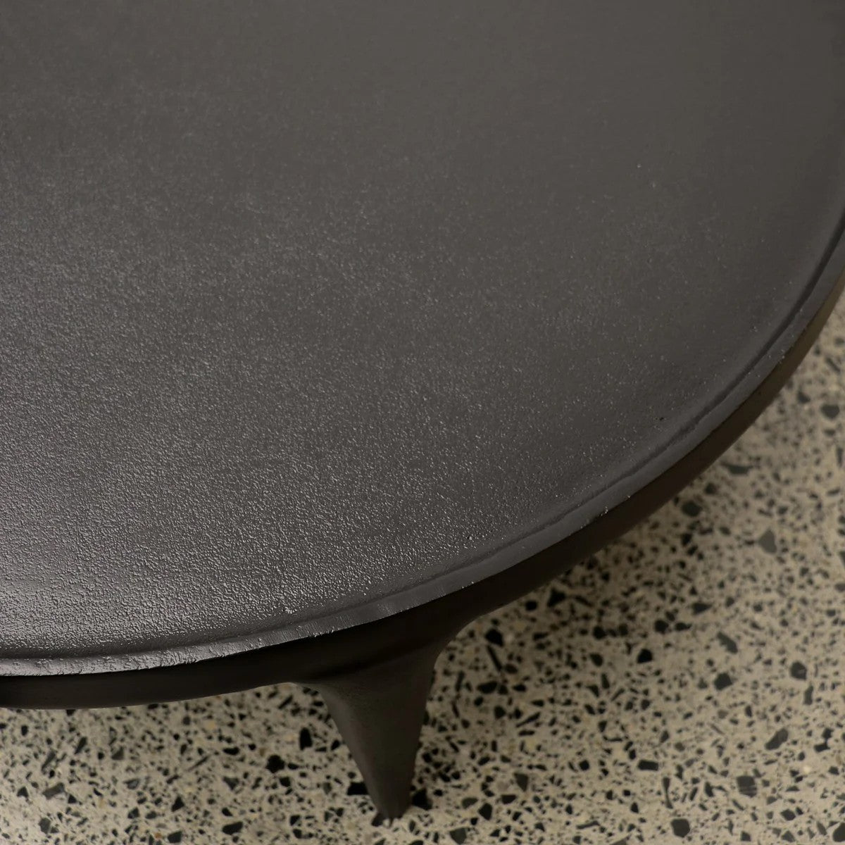 Round black coffee table with a textured surface on a terrazzo floor.
