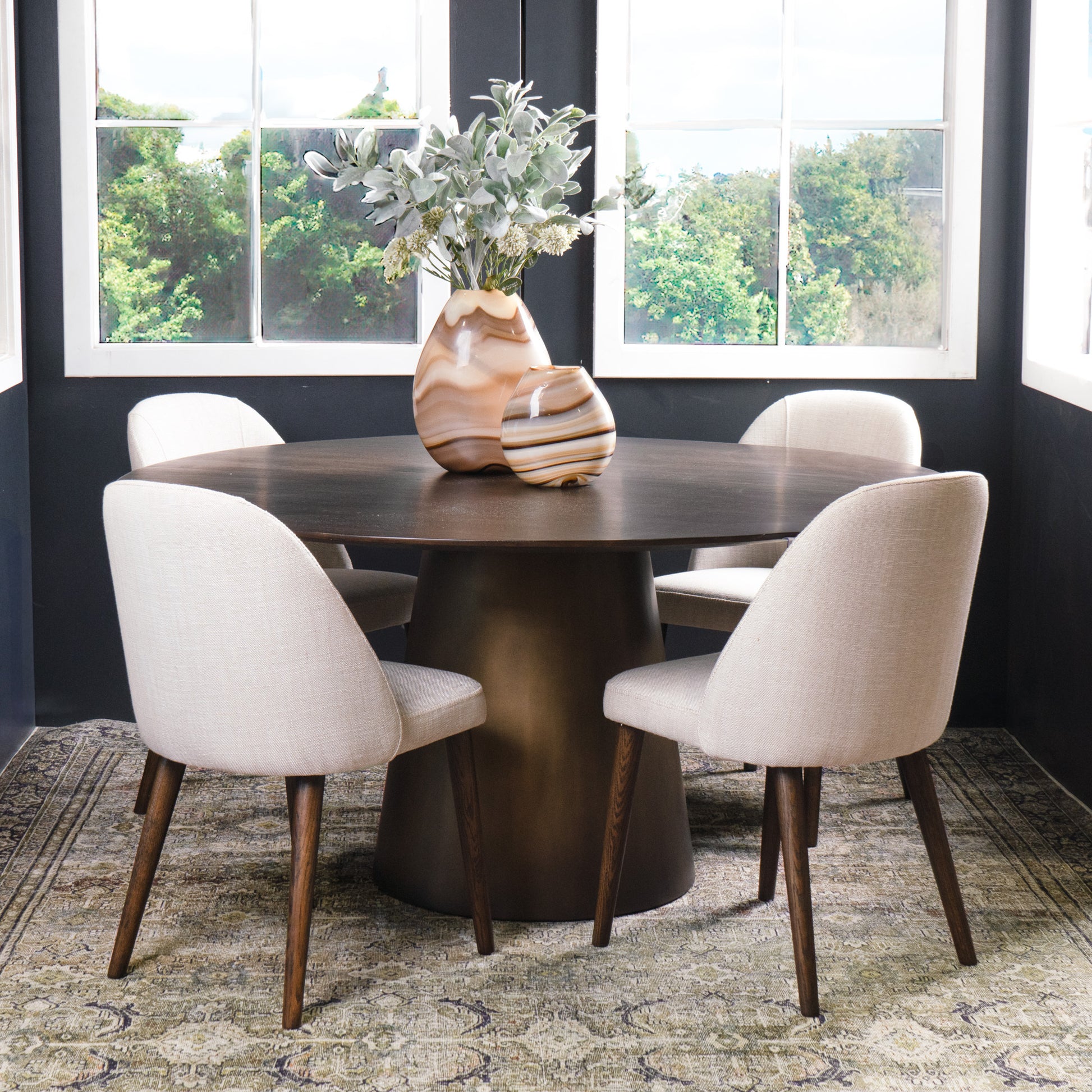 Dining room with a round wooden table and four beige chairs, featuring a vase with flowers on the table.