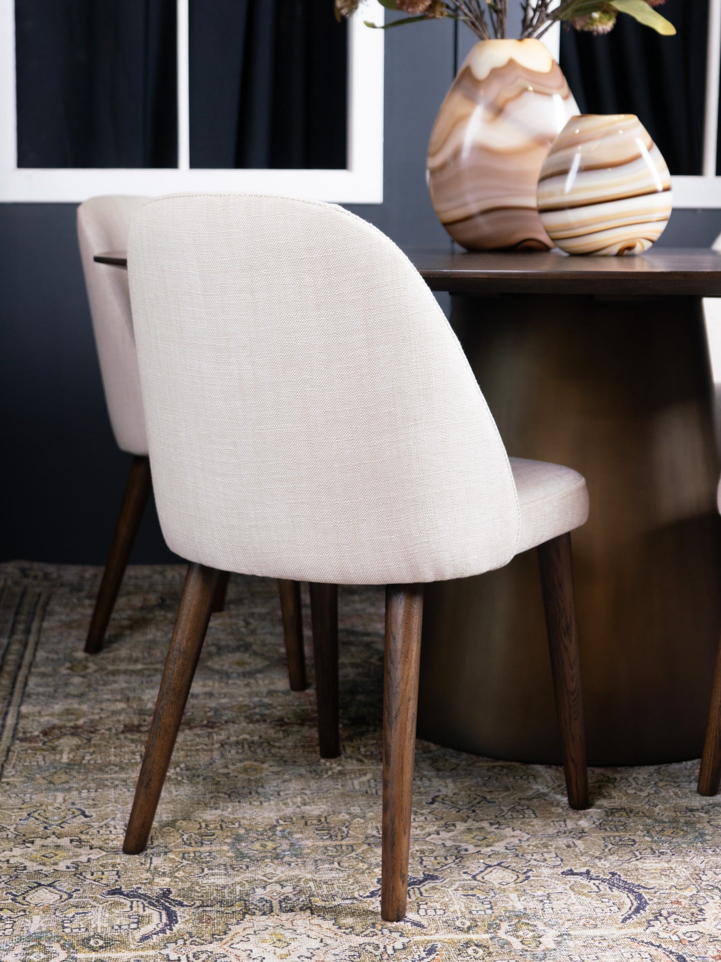 Beige chair with wooden legs in a room with a dark wall and patterned rug.