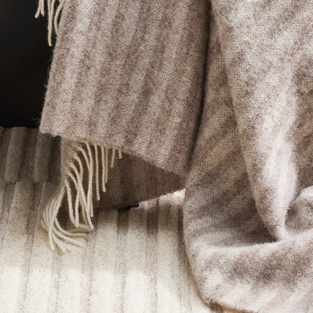 Close-up of a textured oatmeal coloured throw blanket with fringe on a dark background