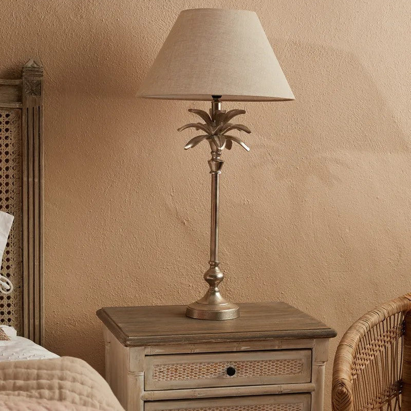 Table lamp with palm tree design on a wooden nightstand against a beige wall.