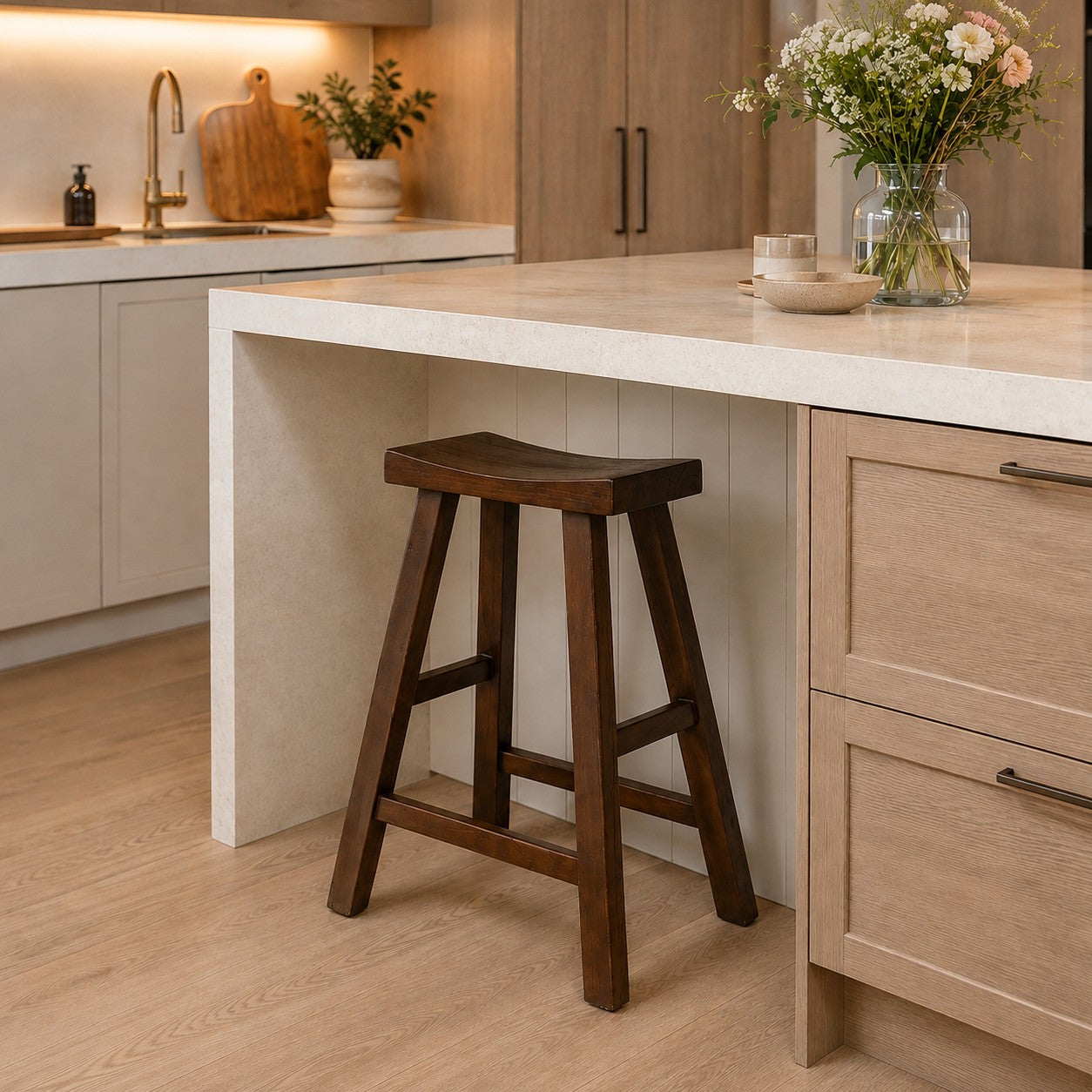 A dark brown wooden bar stool with a curved seat and four legs, positioned in a modern kitchen next to a light wood island counter.