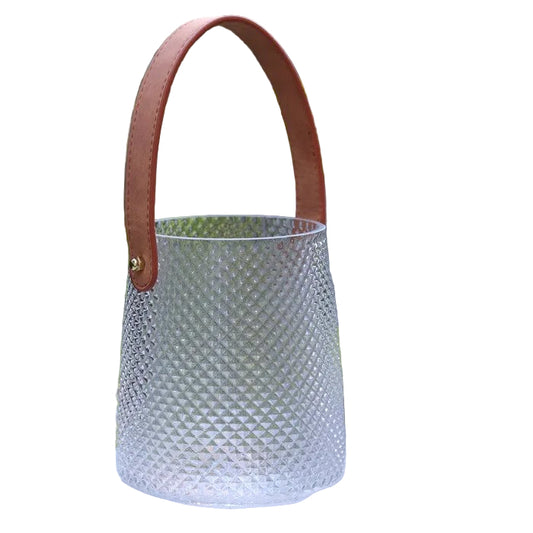 Textured glass hurricane with a brown faux leather handle in a garden setting