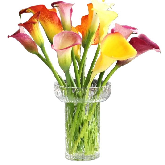 Clear glass vase with colorful calla lilies on a white surface with a gray couch in the background