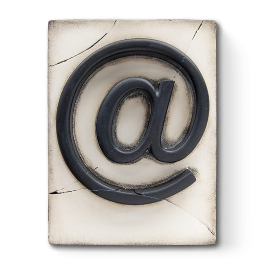 A decorative plaster plaque featuring the symbol 'at' in a cracked black finish, with silver and gold leafing details.