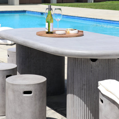 Concrete outdoor table with a bottle of wine, glasses, and snacks by a pool.