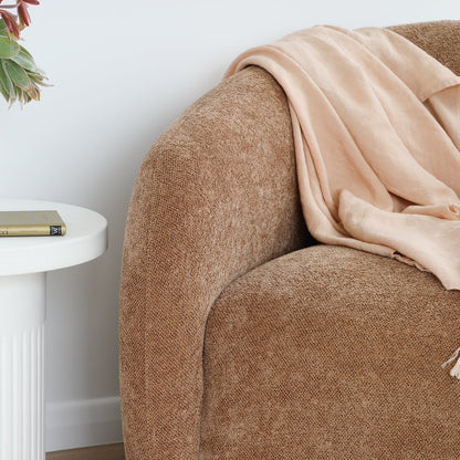 Caramel textured armchair with a beige throw draped over it, next to a white side table with a book.