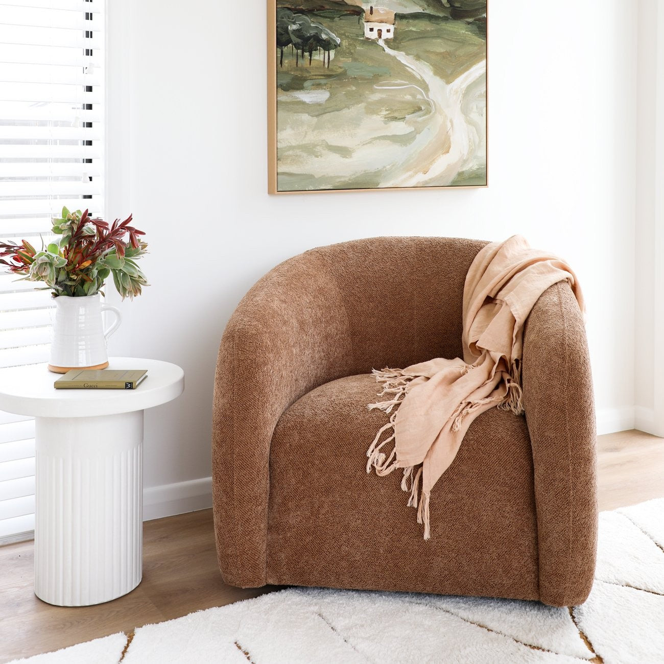 Caramel armchair with a beige blanket in a room with a painting on the wall.