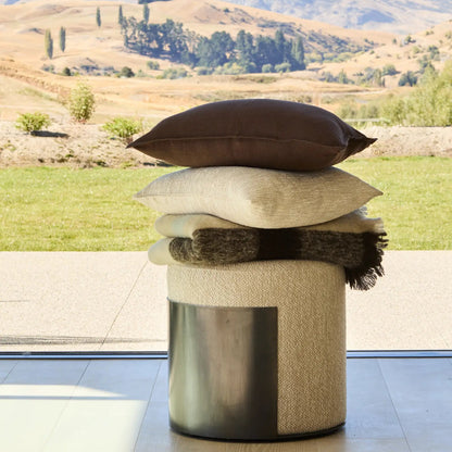 Decorative stool with cushions and a blanket against a scenic outdoor background