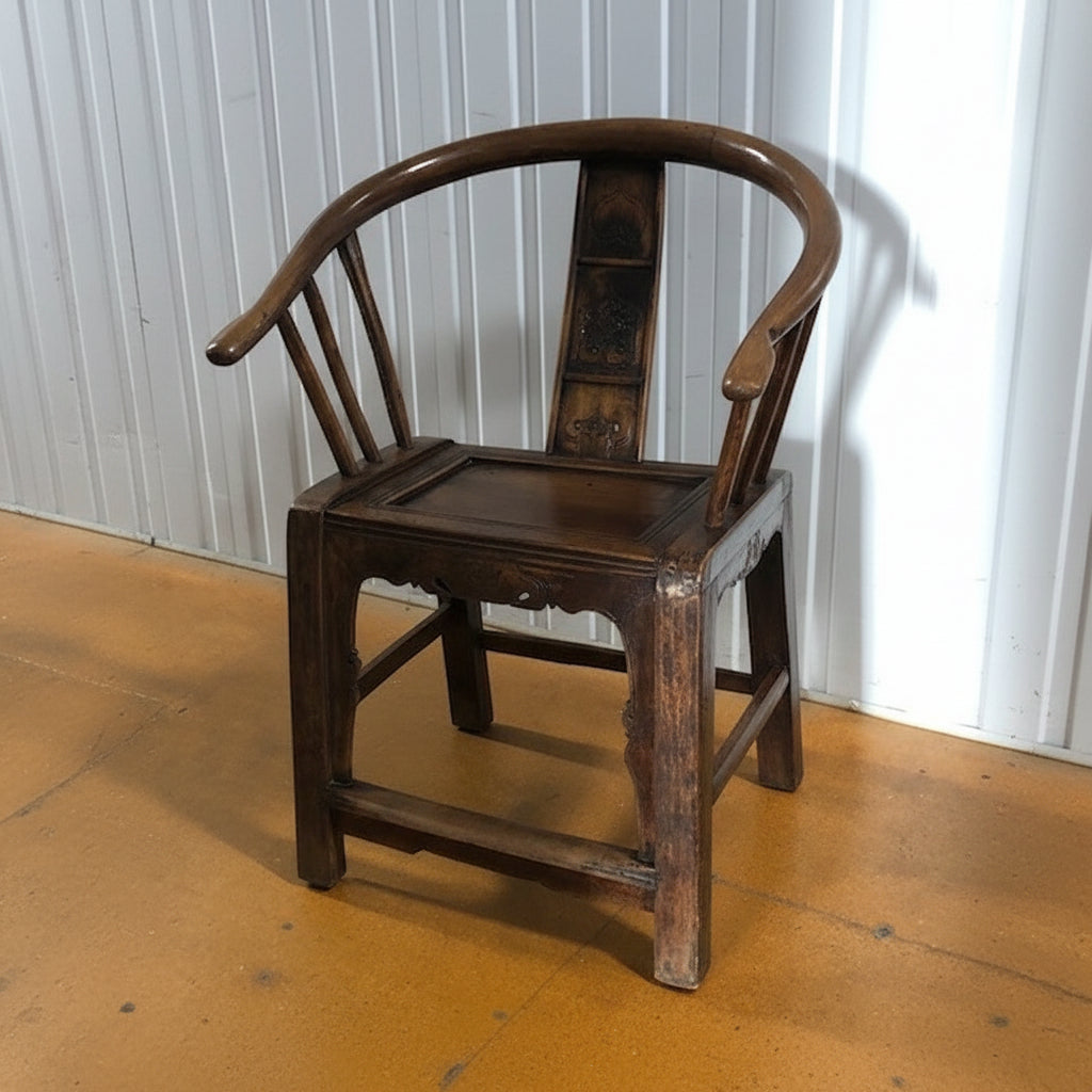 Wooden Horseshoe Chair with curved detailing on a wooden floor against a white panelled wall.
