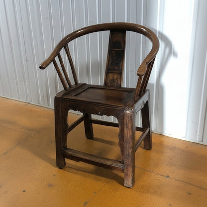 Wooden Horseshoe Chair with curved detailing on a wooden floor against a white panelled wall.