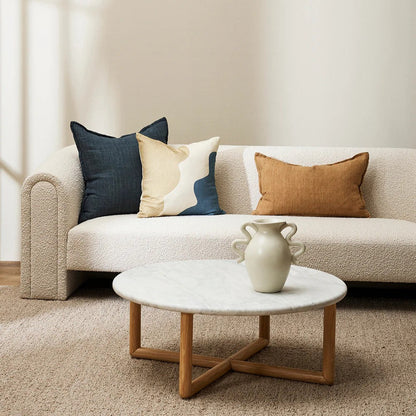 Beige boucle sofa with a cumin linen cushion and other decorative cushions with a marble top coffee table in a living room setting. 