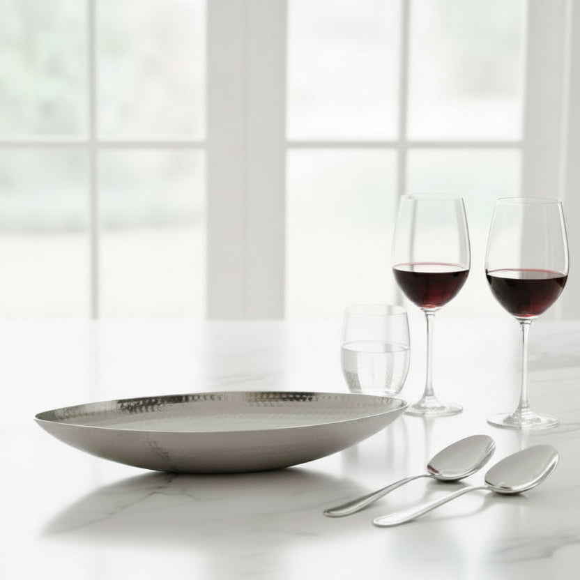 oval serving dish on white marble bench top with wine glasses and serving spoons 