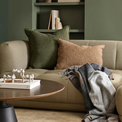 Cosy living room with a beige sofa, green and brown pillows, a brown and grey plaid throw and a wooden coffee table.
