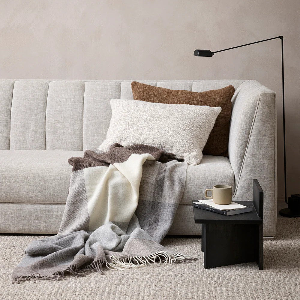 Grey sofa with a plaid throw blanket and scatter cushions in a living room setting.