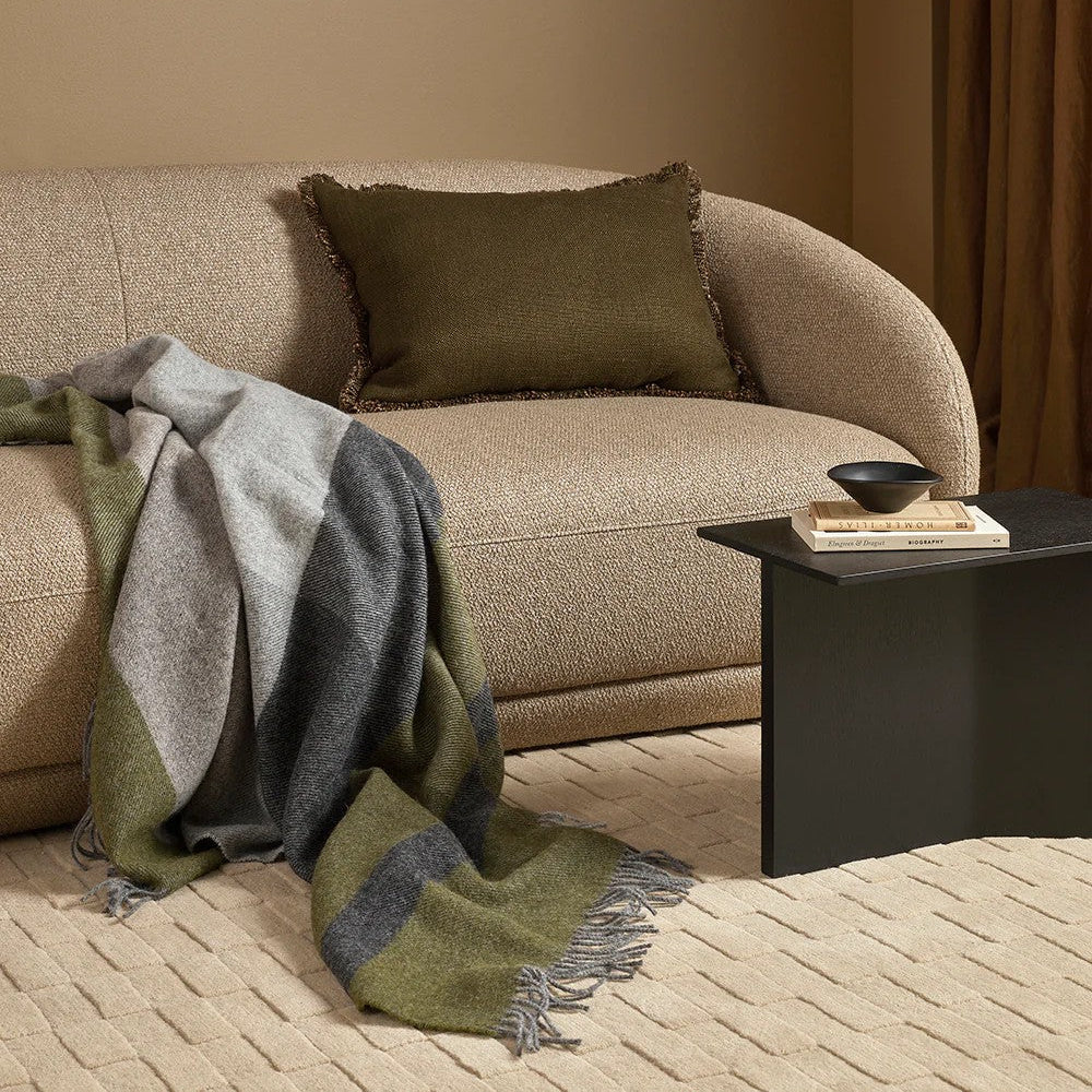 Beige sofa with a green and grey throw blanket and brown pillow in a living room setting.