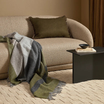 Beige sofa with a green and grey throw blanket and brown pillow in a living room setting.