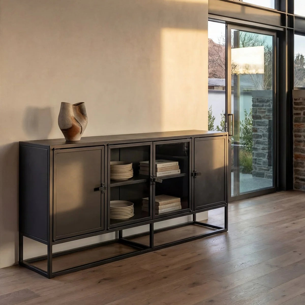 Modern black sideboard with decorative items in a room with wooden flooring and a sliding glass door.