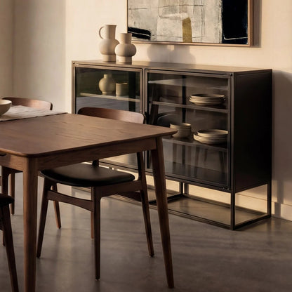 A dark wood dining table with matching chairs is shown in a styled dining room next to a black glass-front sideboard cabinet with metal legs.