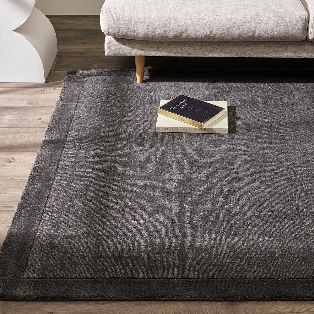 Charcoal floor rug on a wooden floor with a beige sofa and decorative pillows in the background.