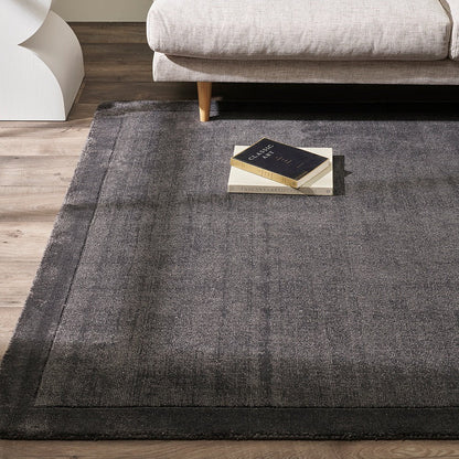 Charcoal floor rug on a wooden floor with a beige sofa and decorative pillows in the background.