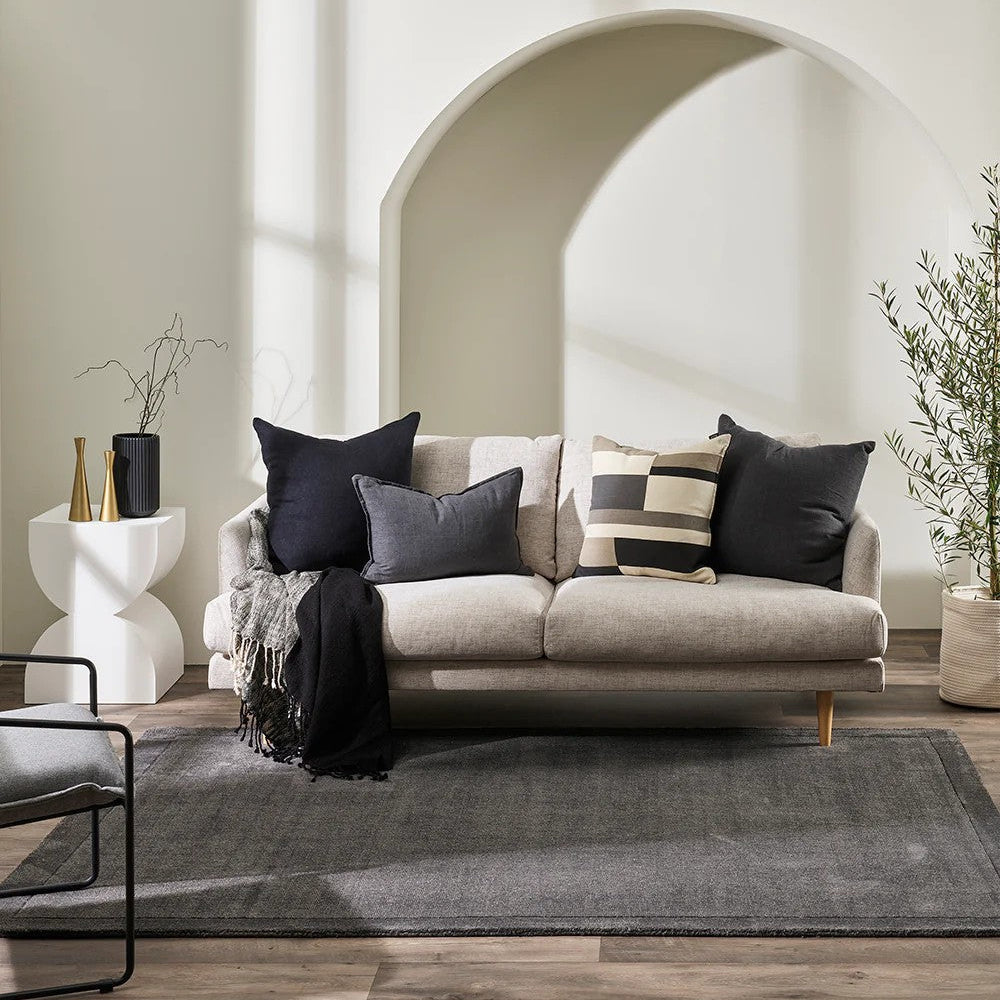Modern living room with a linen sofa, decorative pillows, sitting on a charcoal floor rug.
