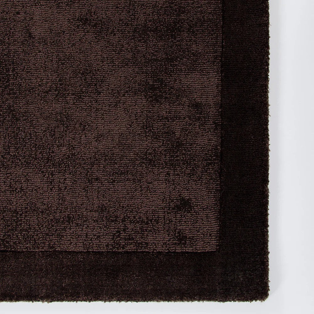 Close-up of a chocolate brown textured rug corner on a white background
