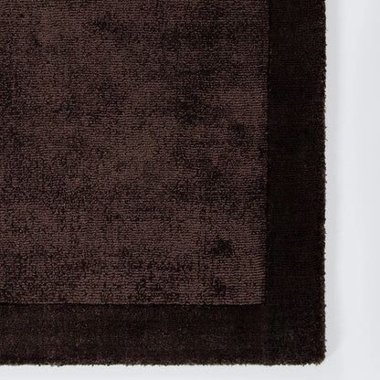 Close-up of a chocolate brown textured rug corner on a white background