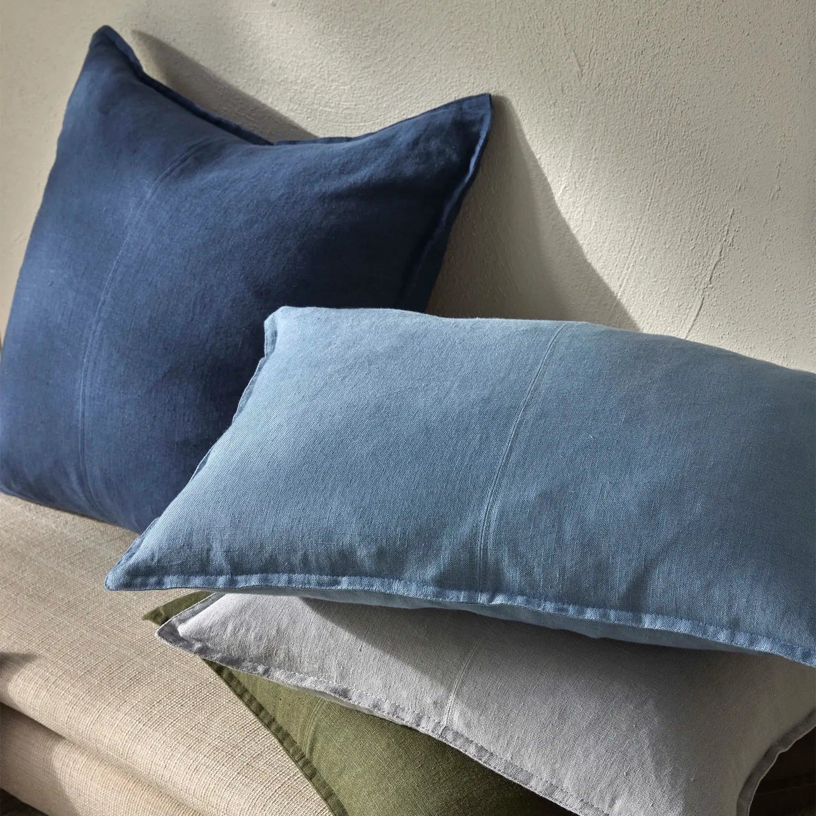 Three pillows in blue, gray, and green on a beige surface