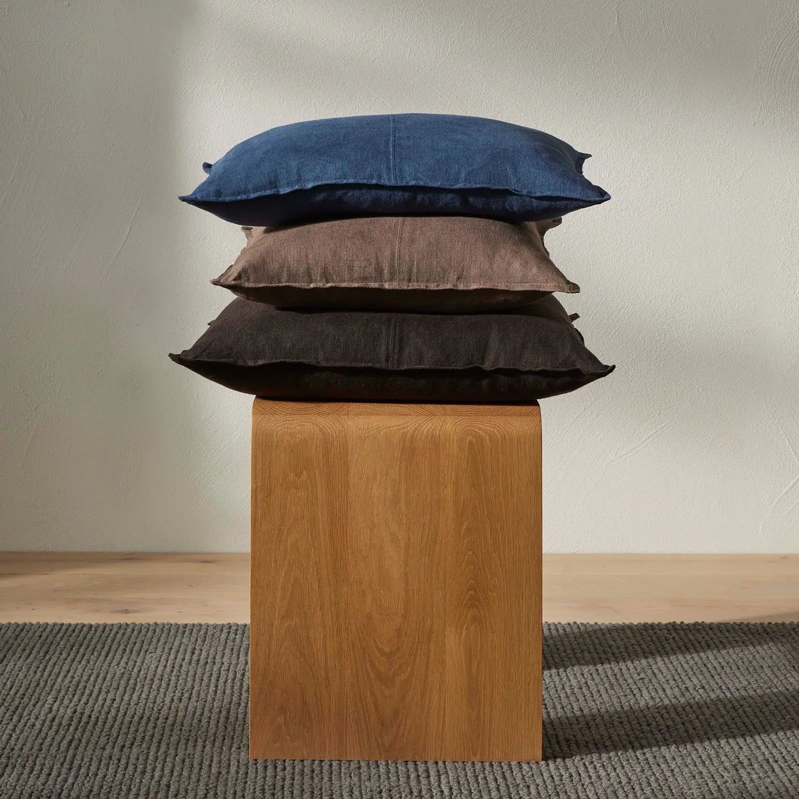 Stack of three pillows on a wooden block against a plain wall.