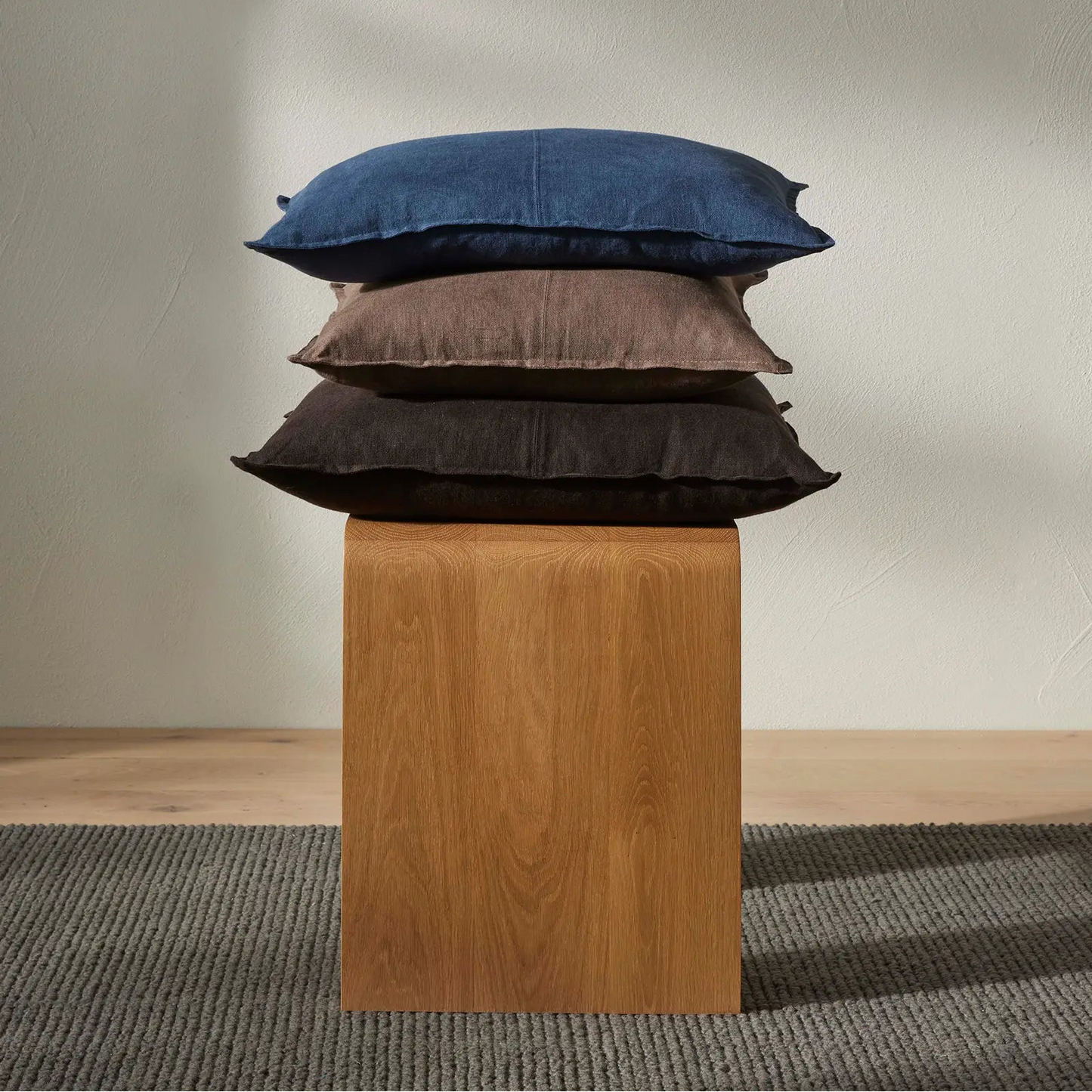 Stack of three pillows on a wooden block against a plain wall.