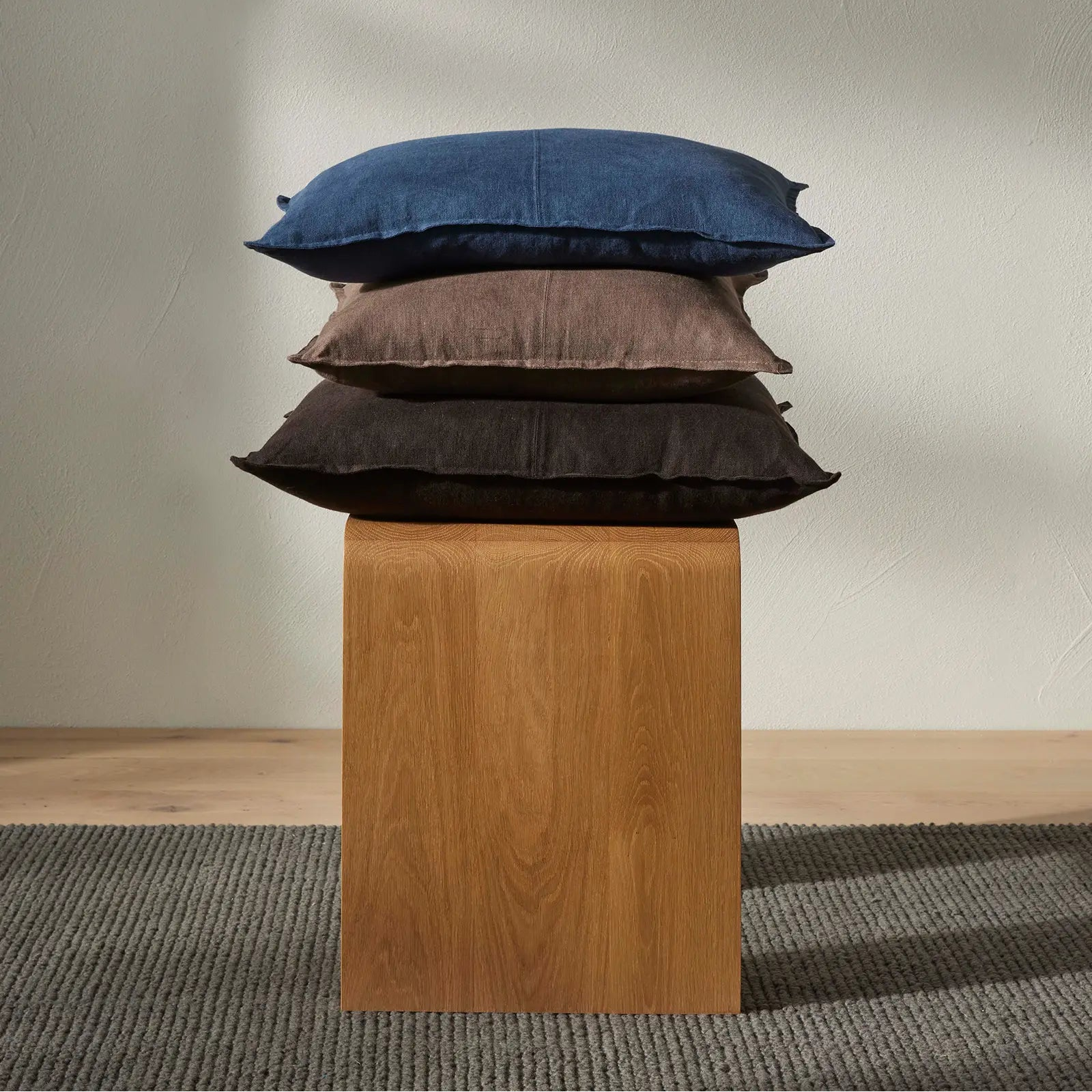Stack of three pillows on a wooden block against a plain wall.