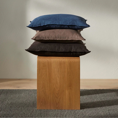 Stack of three pillows on a wooden block against a plain wall.