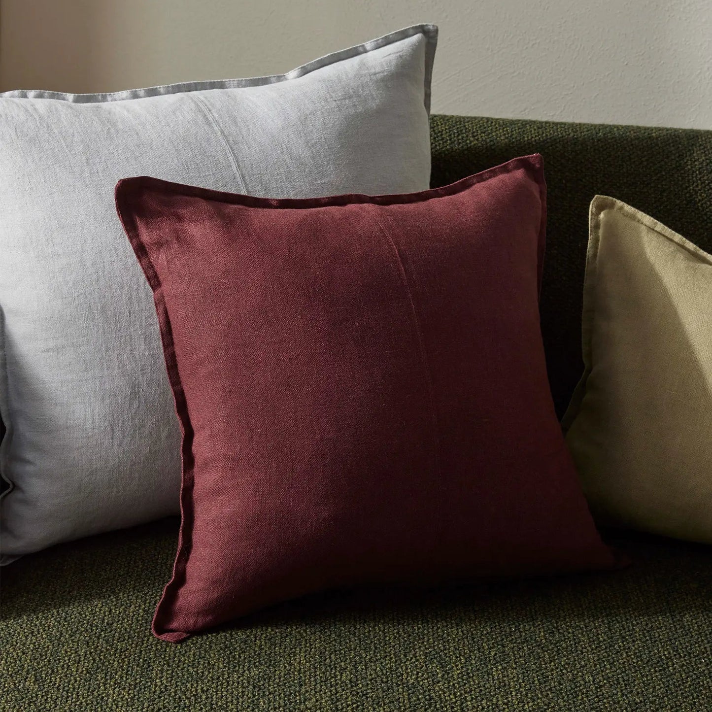Three pillows in red, gray, and beige on a green sofa against a neutral wall.